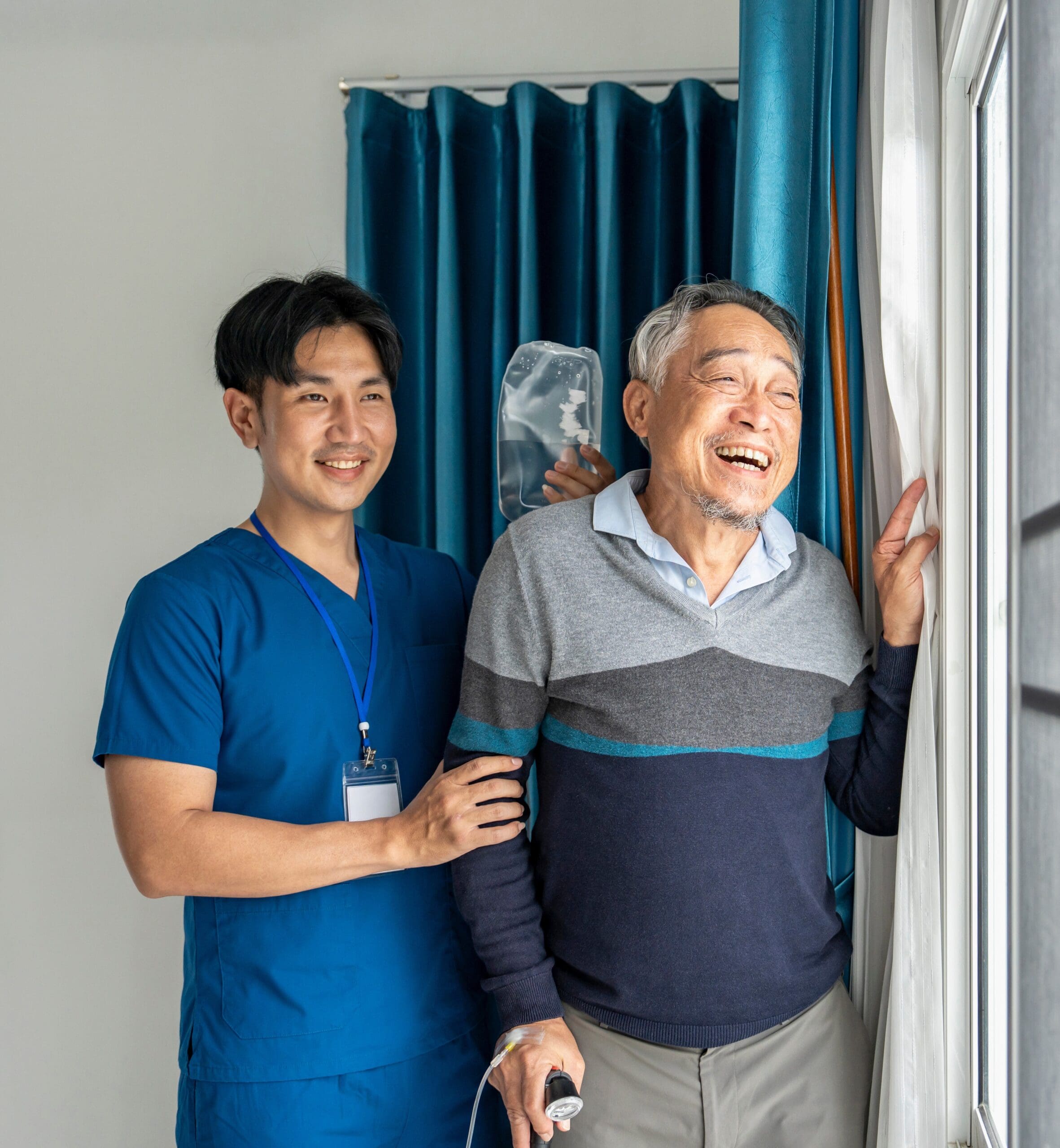 Nurse supporting elderly man receiving IV therapy while standing by window